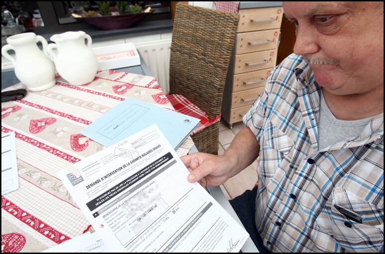 A former carpenter with respiratory cancer who can no longer work shows his health dossier.